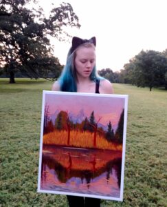 Rachel holding one of her paintings at a park.